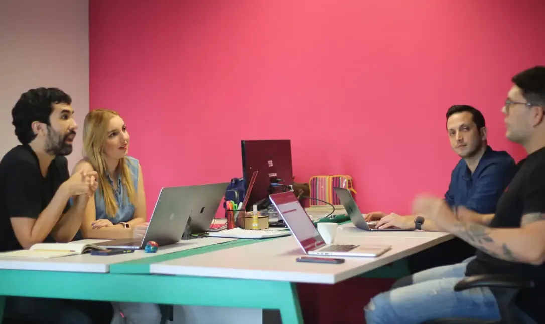 Four Koombea teammates in conversation across two desks, laptops open between them